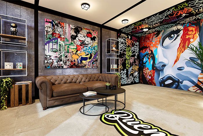 Interior de la tienda Buenahierba – Estilo urbano y arte callejero Interior de la tienda Buenahierba con decoración moderna de estilo urbano, grafitis coloridos en las paredes, sofá de cuero marrón y obras de arte contemporáneo, reflejando la identidad joven y creativa de la marca CBD.